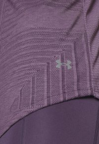 Violetti urheilupaita, jossa on teksturoitu kangas vaakasuorilla ja pystysuorilla kuvioilla, sekä vaaleanharmaa logo oikeassa alareunassa.