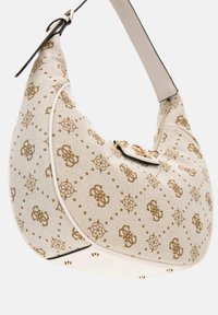 Crème canvas tas met goud logo patroon, gebogen vorm, zwarte afwerking, gouden hardware accenten en een enkele verstelbare schouderriem.
