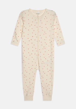 Combinaison une pièce beige clair avec des manches longues, ornée d'un motif répétitif de petits cœurs roses et d'une fermeture éclair sur le devant.