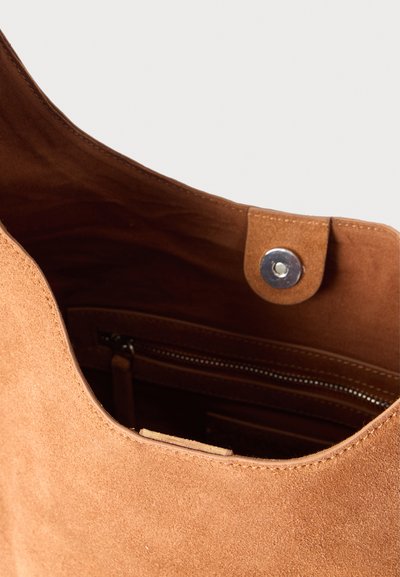 Καφέ σουέτ τσάντα χειρός ανοιχτή που δείχνει το σκοτεινό εσωτερικό και την τσέπη με φερμουάρ με μεταλλικό κλείσιμο με πατάκι στην κορυφή.