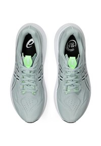 Ljusgrå sportskor med texturerad mesh-ovandel, svarta detaljer, snörning och en vadderad vit sula. Grön detalj på tungan.