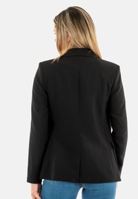 Blazer negro con un diseño ajustado, solapas ejercidas y confección a medida. Cuenta con dos bolsillos y una costura central en la parte posterior.