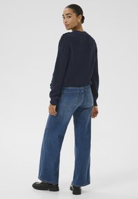 Navy knitted sweater with ribbed texture, paired with light blue wide-leg jeans and shiny black shoes; features round neckline and loose fit.