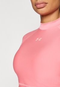 Ροζ αθλητικό τοπ με μακριά μανίκια, κατασκευασμένο από λείο, ελαστικό ύφασμα· διαθέτει εφαρμοστή σχεδίαση και διακριτικό λογότυπο στο στήθος.