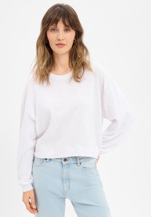 Felpa bianca corta con maniche lunghe e scollo rotondo, abbinata a jeans azzurri a vita alta. Tessuto morbido e strutturato.