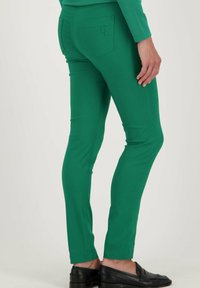 Groene slim-fit broek met een soepele textuur, voorzien van een achterzak met een logo. Het ontwerp is figuurvormend en taps toelopend bij de enkel.