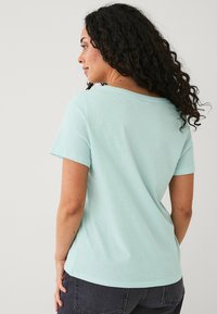 Mintgroene t-shirt met korte mouwen, gemaakt van zachte katoen. Het heeft een ontspannen pasvorm, ronde halslijn en een gladde textuur met minimale details.