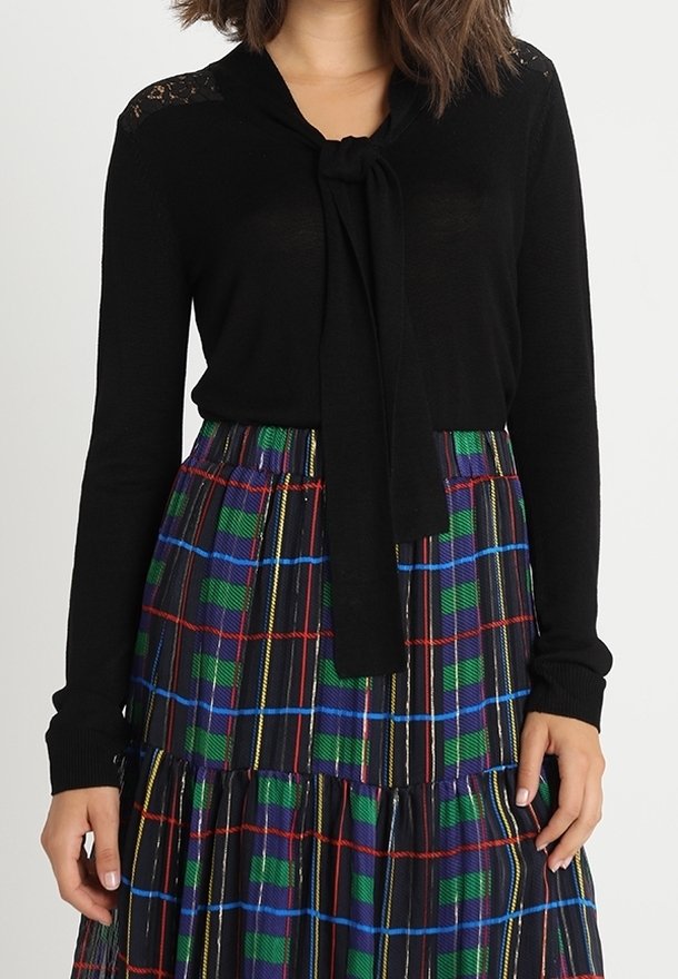 Svart stickad topp med en knytning vid halslinningen och spetsdetaljer. Matchad med en lager-på-lager rutiga kjol i grön, blå, röd och svart.