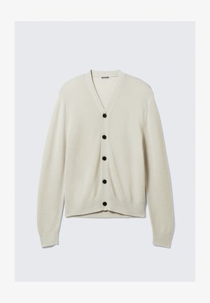 Beige cardigan med V-hals, langermet og svarte knapper foran. Strikket tekstur, tettsittende stil, glatt stoff. Merkeetikett synlig.