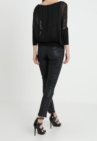 Top nero semi-trasparente con righe verticali, abbinato a pantaloni in pelle nera aderenti e sandali con tacco a strappo neri.