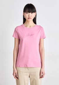 Pink cotton t-shirt with short sleeves and a crew neck. Features a cursive embroidered design on the chest area. Smooth texture.