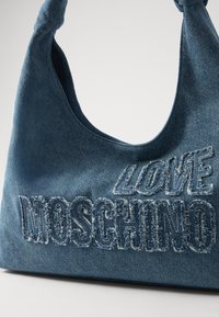 Denim-håndveske med en knyttet håndtak, dekorert med "LOVE MOSCHINO" i slitt brodert skrift. Mørkeblå farge med en myk tekstur.