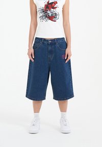 Denim shorts in dark blue with a loose silhouette and knee-length hem. Features front pockets and a small pink embroidered detail.