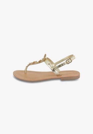 Gold flat sandals with a toe strap and ankle strap, featuring decorative embellishments. The sole is light tan with stitching accents.