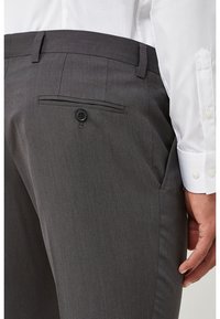 Pantalones grises a medida con una textura suave, que cuentan con un bolsillo trasero abotonado y sutiles detalles de costura, combinados con una camisa blanca.