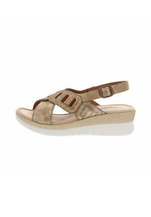 Sandale beige à bout ouvert avec bride de cheville réglable, semelle rembourrée, motifs géométriques ajourés et talon compensé blanc.