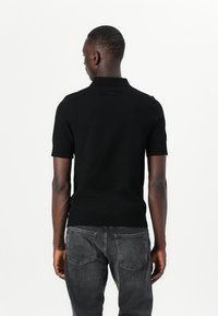 Svart kortermet polo skjorte laget av glatt stoff, med en klassisk krage og en logo detalj på ryggen, kombinert med mørke jeans.