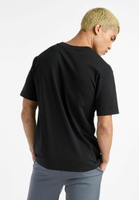 Camiseta de algodón negra con escote redondo y mangas cortas, con un corte relajado y un detalle de costura mínima en el dobladillo.