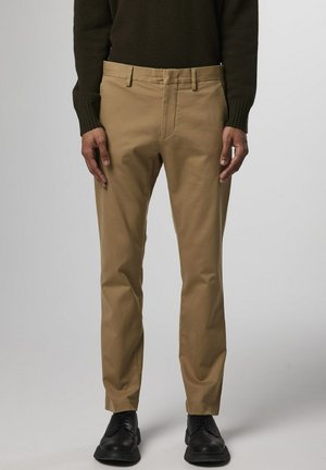 Beige chinos with a slim fit, featuring a flat front, standard pockets, and belt loops, styled with black shoes and a dark knit sweater.