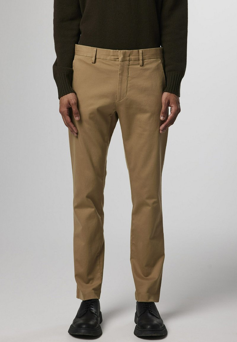 Beige chinos met een slim fit, met een platte voorkant, standaardzakken en riemlussen, gestyled met zwarte schoenen en een donkere gebreide trui.