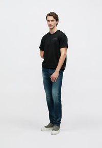 Must lühikeste varrukatega T-särk, teksassinised teksad, rohelised tossud. Modell seisab neutraalses poosis tavalise tausta ees. Lihtne disain.