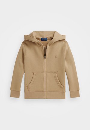 Sudadera con cremallera en tono beige, hecha de tela texturizada, que cuenta con una cremallera delantera, dos bolsillos frontales y una capucha con un logo bordado en el pecho.