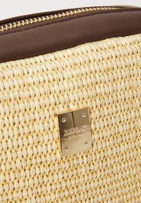 Borsa in paglia intrecciata con una placca logo dorata, rifiniture in finta pelle marrone e una cerniera dorata. Superficie testurizzata con una palette di colori naturali.