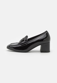 Chaussures à talon carré en cuir verni noir avec un bout pointu et une bride décorative sur le dessus. Texture lisse et finition brillante.