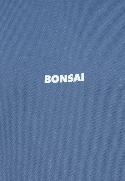 Zila adīta auduma ar smalku tekstūru, centrā ar lieliem baltajiem burtiem ir vārds "BONSAI".
