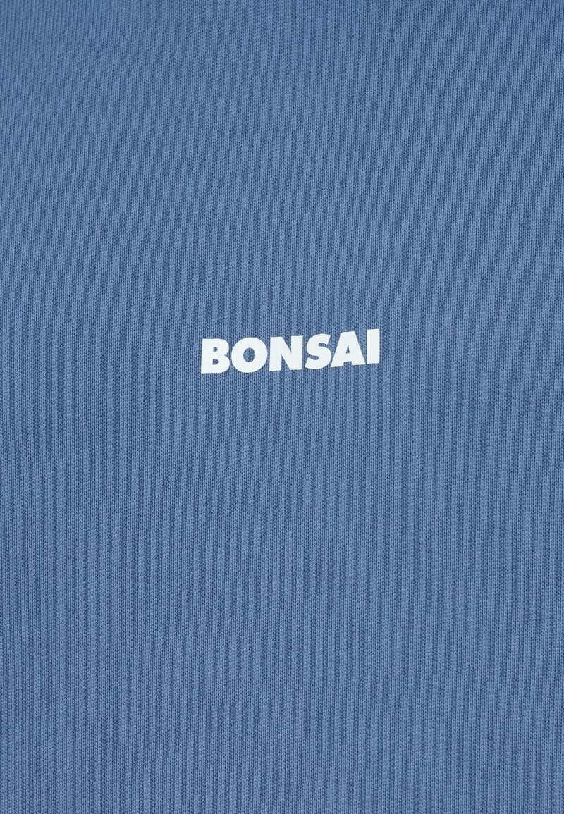 Tissu en tricot bleu avec une texture subtile portant le mot "BONSAI" en lettres blanches en gras au centre.