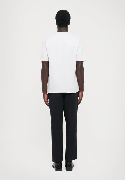 Biała koszulka z krótkim rękawem z dekoltem typu crew. Połączona z czarnymi spodniami o prostym kroju i czarnymi butami. Prosty design, bez wzorów.