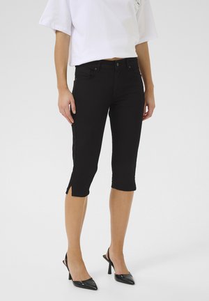 Jeans capri neri con un design aderente, caratterizzati da spacchi laterali all'orlo e una sottile texture. Abbinati a tacchi a punta nera.