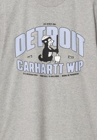 Camiseta de algodón gris con un personaje de dibujos animados con una pala, el texto "DETROIT" y "CARHARTT WIP", y elementos de diseño adicionales en azul y negro.