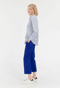 Chemise blanche à boutons avec motif floral bleu, associée à un pantalon cropped bleu et des baskets blanches avec des accents noirs.