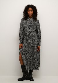 Robe à motif noir et blanc avec des manches longues, fermeture boutonnée à l'avant et ceinture à la taille ; présente des fentes sur les côtés et une silhouette fluide.