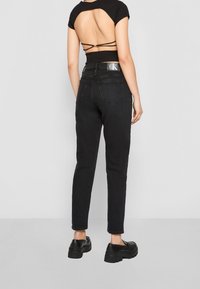 Jeans ajustados negros combinados con una blusa negra que presenta un corte en la espalda y tirantes entrecruzados. La modelo lleva zapatos gruesos negros.