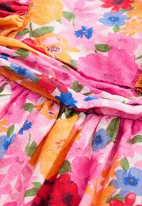 Gros plan sur un tissu rose avec des sections froncées et un imprimé floral coloré en rouge, bleu, orange et feuilles vertes.