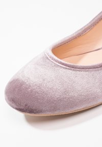 Mjukt rosa sammetsballerinaskor med rund tå och beige innersula på en vit bakgrund.