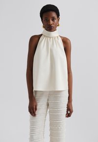 Kermansetti halter top kanssa kokoon kerätty kaula-aukko, yhdistettynä kevyisiin, frangoituihin housuihin, joissa on vaakasuorat raidat. Silkkinen kangas.