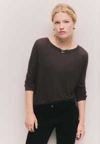 Rudas, dryžuotas, ilgomis rankovėmis viršus su plačia iškirpte, derinamas su juodomis kelnėmis. Aprangą pabrėžia auksinė grandinėlė ir auskarai.