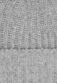 Grijze gebreide beanie met een geribbelde textuur. Zichtbaar kabelpatroon en een omgeslagen manchet aan de onderkant. Zacht, wolachtig materiaal.