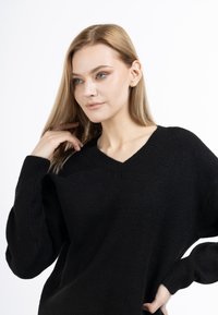 Black sweater with a V-neck, loose fit, and ribbed cuffs. Made of soft, textured fabric, featuring a subtle design detail along the shoulders.