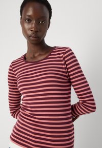 Top aderente a maniche lunghe in rosso scuro e rosa a righe orizzontali, con scollatura tonda e tessuto liscio e elasticizzato.