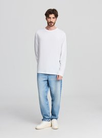 Biała koszula z długim rękawem, bawełniany materiał, okrągły dekolt; zestawiona z jasnoniebieskimi luźnymi dżinsami i białymi trampkami. Prosty, casualowy design.