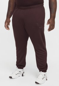Mörkröda Nike sweatpants med elastisk midja, sidofickor och tapered muddar. Diskret ton-i-ton logotypdetalj på vänster ben.