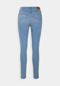 Blaue, enge Skinny Jeans aus Denim mit hohem Bund, zwei Gesäßtaschen und einem Leder-Patch am hinteren Bund. Glatte Textur, klassisches Design.