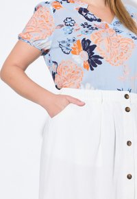 Bloemige blouse in lichtblauw, met oranje en marineblauwe patronen. Paar witte shorts met een textuurafwerking en bruine knopen.