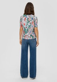 Krótki rękaw top w kwiatowy wzór w kolorze zielonym, czerwonym, niebieskim i białym; połączony z szerokimi, ciemnoniebieskimi dżinsami; strukturalny i dopasowany krój.