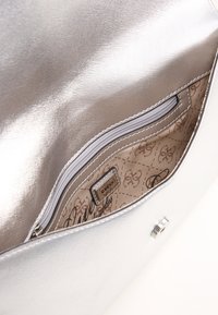 Srebrna kopertówka wykonana z teksturowanego materiału syntetycznego. Posiada kieszeń na zamek błyskawiczny i wzorzyste wnętrze, z logo "GUESS".