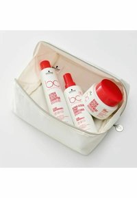 Väsk med vit kosmetik i silverdragkedja innehåller tre hårvårdsprodukter: två sprayflaskor och en burk, alla med röda detaljer och text.